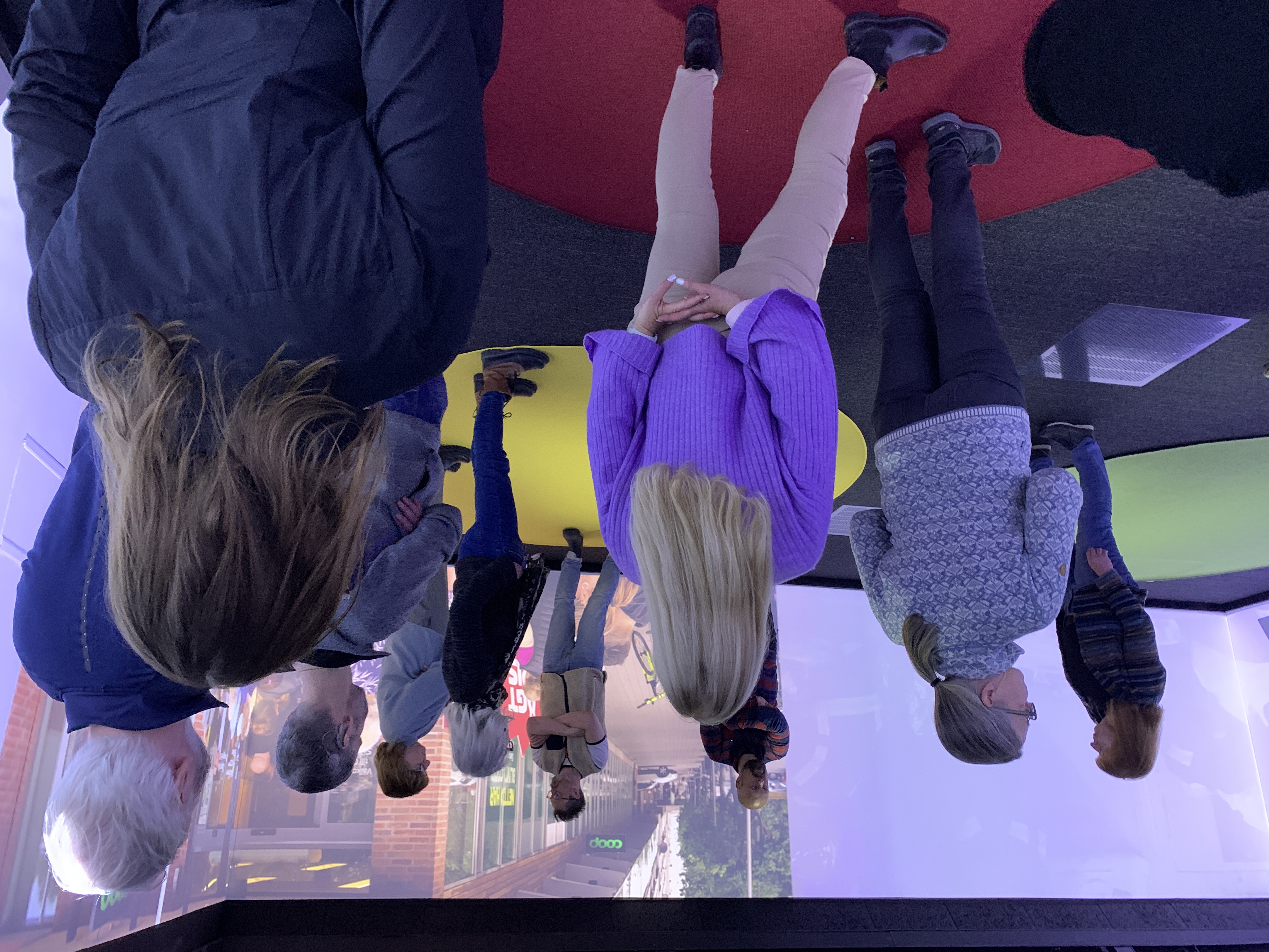 A group of people standing in a room with a large screen displaying an urban environment.